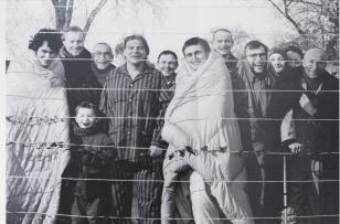 Czarno białe zdjęcie przedstawiające grupę trzynastu osób, mężczyzn, dwie kobiety i dziecko, stoją frontem do obiektywu, sześć osób w pierwszym rzędzie – reszta tłocząc się za nimi, na pierwszym planie sznurek do prania.