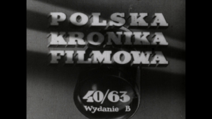 Kadr otwierający film. Jest nim czołówka Polskiej Kroniki Filmowej. Film czarno-biały. Widać tytuł trzy wyrazy: na górze Polska, niżej Kronika, na dole Filmowa. W tle widać okrągły obiektyw kamery, którego szklana część znajduje się u dołu ekranu. Na obie