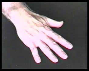 Kadr wypełnia spoczywająca na czarnej powierzchni dłoń męska. Jest duża, ma dobrze widoczne żyły. Bez obrączki.