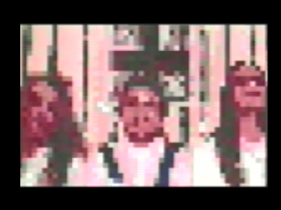 Kadr z filmu przedstawiający rozpikselowany obraz trzech osób widocznych do ramion, znajdujących się w pomieszczeniu..