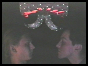 Kadr z filmu, dwie postacie zwrócone twarzami do siebie, nad nimi forma z elementami świetlnymi.