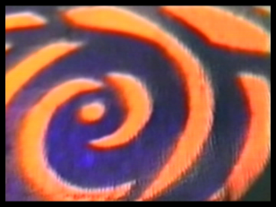 Kadr z filmu, przedstawiający geometryczne, układające się koliście ornamenty w pomarańczowym kolorze, na niebieskim tle.