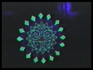Kadr z filmu, przedstawiający fluorescencyjny zgeometryzowany okrągły kształt na ciemnych tle.