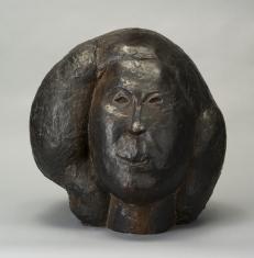Rzeźba - odlew z brązu. Przypomina owalny, brązowy kamień. Na wprost widać rysy twarzy - oczy, nos, usta.