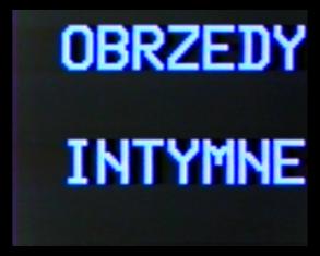 Kadr tytułowy z filmu - na czarnym tle niebieski, rozpikselowany na krawędziach liter napis: OBRZĘDY INTYMNE.