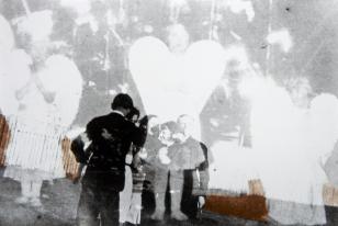 Fotomontaż wykonany z dwóch negatywów przedstawiających trzy dziewczynki w białych strojach z przyczepionymi do pleców skrzydłami oraz poniżej pokazaną w mniejszej skali grupę osób w plenerze.