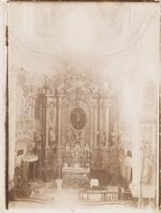 Fotografia w tonacji sepii. Widok wnętrza kościoła - ujęcie na ozdobny ołtarz główny z figurą ukrzyżowanego Chrystusa w centrum.