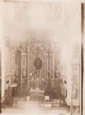 Fotografia w tonacji sepii. Widok wnętrza kościoła - ujęcie na ozdobny ołtarz główny z figurą ukrzyżowanego Chrystusa w centrum.