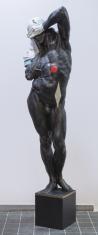 Rzeźba pełna, figuralna, przedstawiająca w kolorze patynowanego na ciemnoszary/czarny brązu. Męski akt nieznacznie ponadnaturalnej wysokości stojący na sześciennym brązowym postumencie. Akt jest ukazany w sposób realistyczny, klasycyzujący, stoi w kontrap