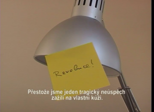 Kadr z filmu przedstawiający lampę z IKEI, do której jest przylepiana, odpadająca żółta karteczka z napisem „Revoluce!” [czes.: rewolucja].