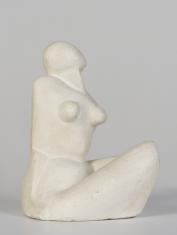 Gipsowa rzeźba przedstawiającą siedzącą kobietę. Kobieta jest przedstawiona w sposób uproszczony, zgeometryzowany. Ma spadziste zaokrąglone ramiona, krągłe piersi, podkreśloną talię, nieco wypukły brzuch, szerokie uda. Artystka nie zaznaczyła na głowie ko