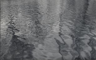 Czarno-biała fotografia w układzie poziomym. Pomarszczona tafla wody, pokrytą na całej powierzchni smugami światła i zygzakowatymi cieniami.