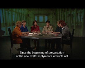Kadr z filmu, wokół stołu umieszczonego w pomieszczeniu o zielonej tonacji na krzesłach siedzi sześć kobiet o różnych kolorach włosów..
