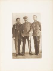 Fotografia portretowa w sepii, kadr pionowy. Trzech mężczyzn w mundurach Wojska Polskiego stojących na wprost widza. Postać w środku na głowie ma czapkę, a w lewej dłoni szablę w jasnej pochwie skierowaną w dół przy lewej nodze.
