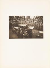 Fotografia w sepii wykonana z wysokości kilku metrów nad ziemią, poziomy kadr. Na pierwszym planie oficerowie Wojska Polskiego wsiadający do samochodu. Na drugim planie duża grupa żołnierzy stojących w mundurach przodem do widza.