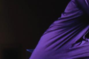 Kadr z filmu - na czarnym tle widoczna środkowa część ciała wygiętego w trakcie tańca, ubranego w fioletową sukienkę. 