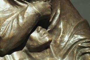 W dużym zbliżeniu fagment rzeźby z brązu - widoczna część twarzy oraz zasłaniające ją ramię. 