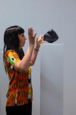 Autorka wystawy Agnieszka Kurant stoi przy czarnej, unoszącej się nad postumentem rzeźbie przypominającej kamień