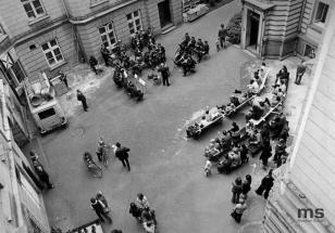 Na czarnobiałym zdjęciu widok z góry na dziedziniec muzeum, na którym zgromadziło się dużo osób, rowerzyści, orkiestra, publiczność na ławkach.