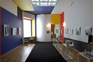 Sala wystawowa z obrazami abstrakcji geometrycznej  ścianami pomalowanymi w prostokątne pola w kolorach granatowym, czerwonym, żtym, białym.