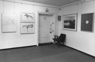 Róg niskiego pomieszczenia. Drzwi z tabliczką Prof. Joseph Beuys, obok fotel. Na ścianach prace artysty o motywach zwierzęcych, zawieszone na cienkich żyłkach. Na podłodze wykładzina. W samym rogu u góry oko kamery przemysłowej