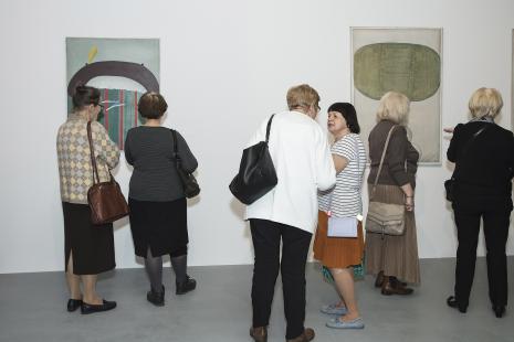 Grupa starszych kobiet z uwagą przypatruje się wiszącym na ścianie abstrakcyjnym obrazom 
