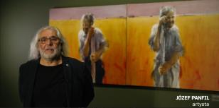 Układ poziomy. Z lewej strony mężczyzna z długimi białymi włosami. Po prawej stronie na zielonej ścianie dwa obrazy w kolorze pomarańczowym.