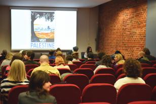 Fotografia pozioma. Duża sala z miękkimi krzesłami ustawionymi w rzędach jak w kinie, na ścianie w głębi na dużym ekranie wyświetlana prezentacja. W fotelach siedzi kilkanaście osób, patrzą na ekran.